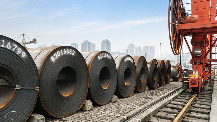 A striking industrial scene, where large steel sheet rolls on tracks against a backdrop of towering city skyline demonstrate the impact of section 232 tariffs on steel industry