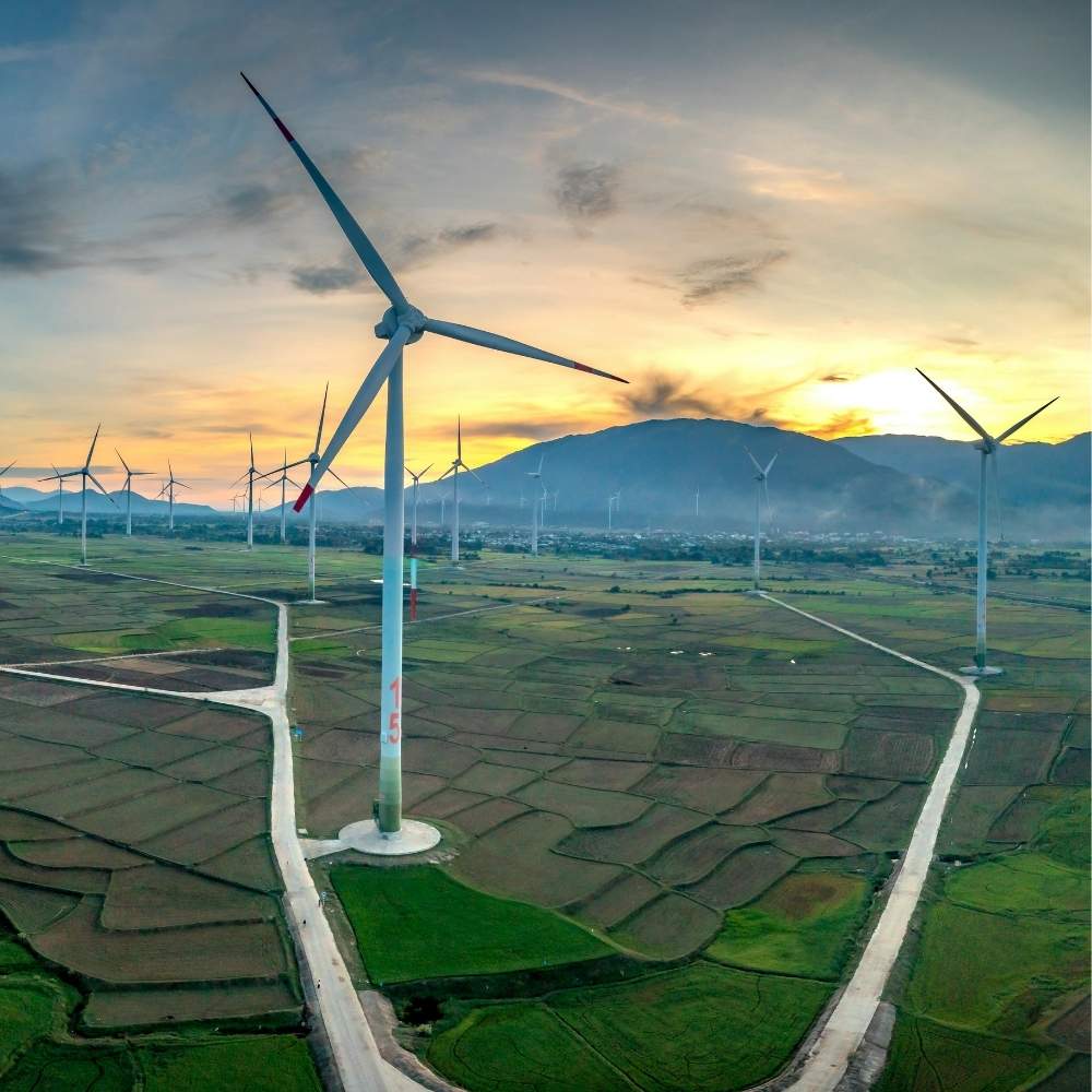 Wind turbines silhouetted against a vibrant sunset in a rural landscape, symbolising CRU's clean technology market intelligence solution.